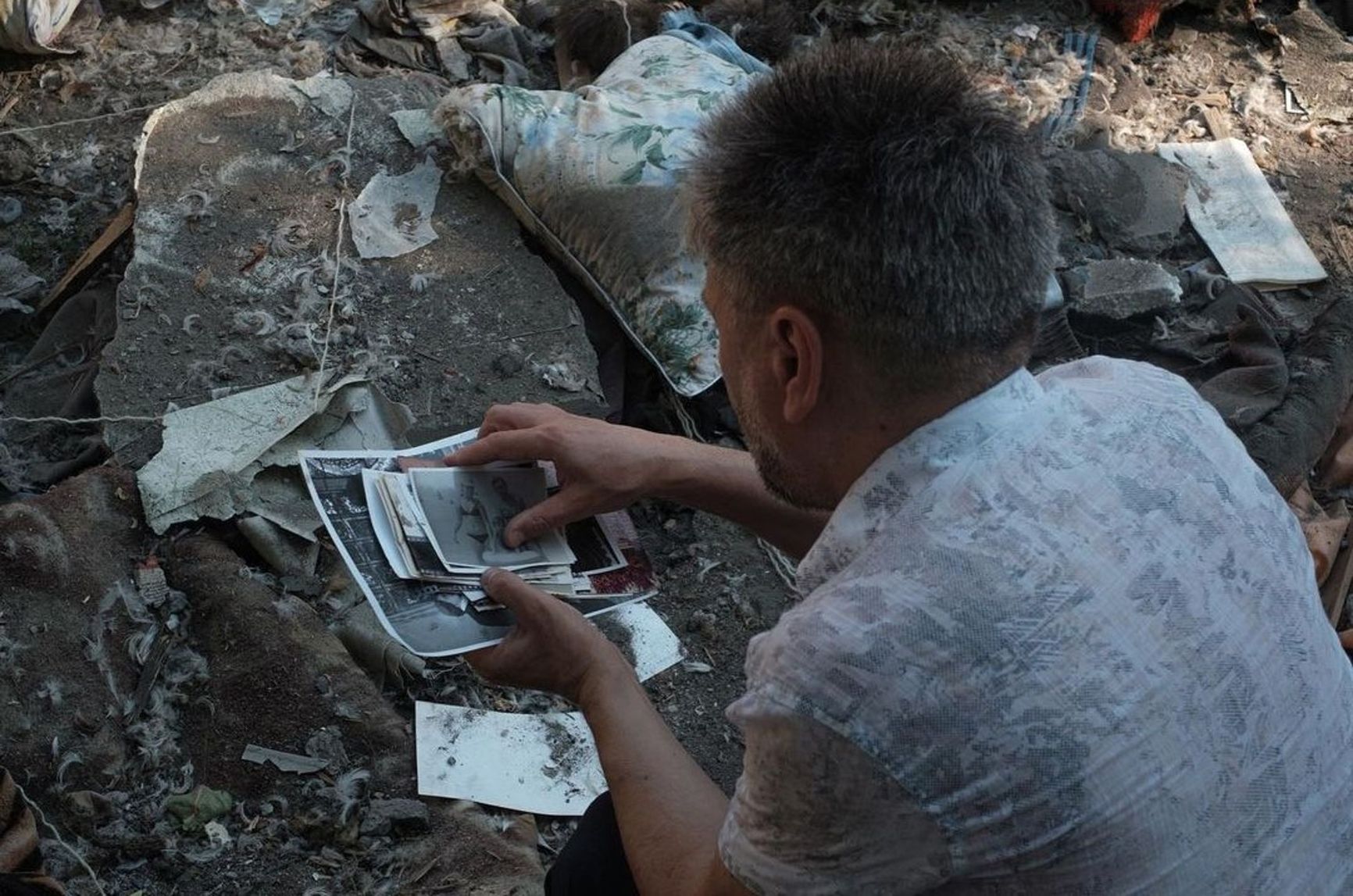 A man collects photographs of his relatives scattered near the destroyed five-story building, Mykolaiv